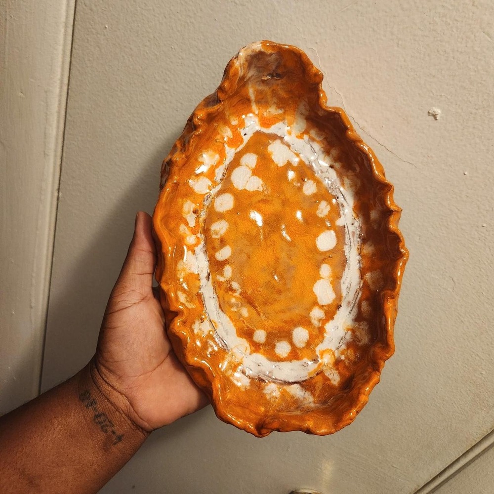 Handmade ceramic trinket dish featuring a rich orange glaze with white accents